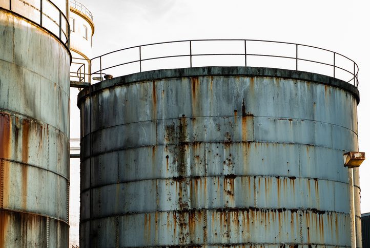 Rusty industrial storage tanks under cloudy sky.